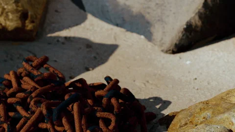 Rusty chain lying on sandy ground near rocks in the afternoon sun Stock Footage 344875360