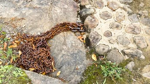 Rusty Chain on Weathered Stone Path with Moss and Grass Stock Photos