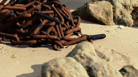 Rusty chains on a sandy beach near rocky formations during daylight Stock Footage 343532696