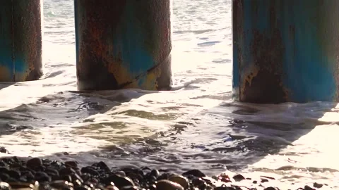 Rusty columns through which the foam wave beats on the rocky beach Stock Footage 174564877