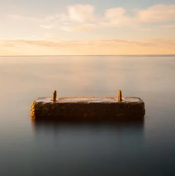 Rusty Concrete Mooring Block Floating in Calm Sea at Sunset 库存照片