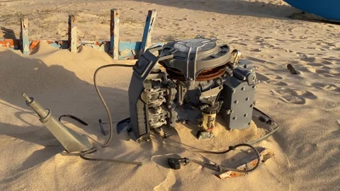 A rusty dismantled boat engine lies partially in the sand on the beach. Stock Footage 302195506