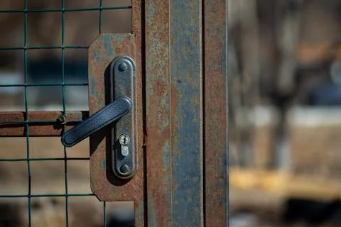 Rusty door, gate closed on a handle-lock with a metal mesh on the street Stock Photos