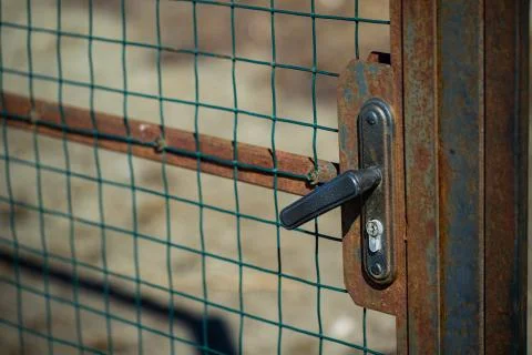 Rusty door, gate closed on a handle-lock with a metal mesh on the street Stock Photos