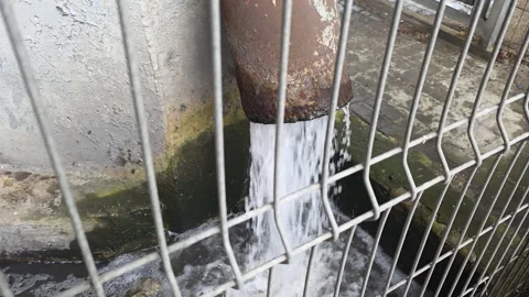 Rusty drainage pipe pouring water into an overflowing urban concrete gutter Video stock 335273391