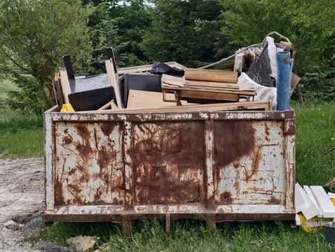 Rusty dumpster filled with trash and debris in grassy outdoor setting Stock Photos