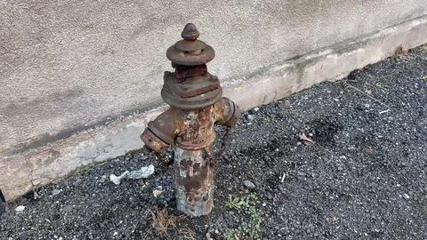 A Rusty Fire Hydrant Positioned Next to a Wall in an Urban Environment or C.. Stock Photos
