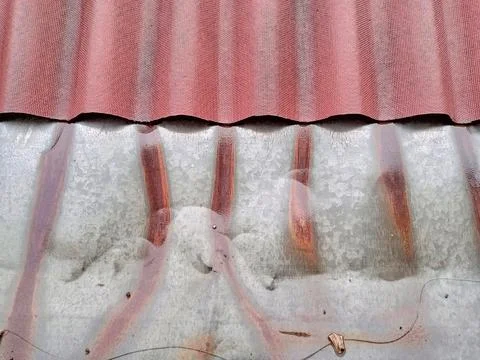 Rusty galvanized metal roofing sheet underneath a red wavy roof tile Stock Photos
