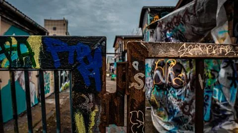 Rusty gate frames vibrant, chaotic graffiti walls Stock Photos
