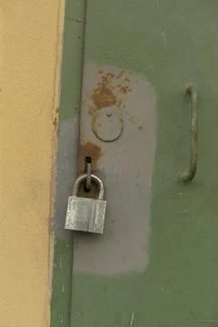 Rusty green latch securing door on sunny yellow wall surface Stock Photos