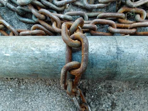 Rusty Iron Chain Wrapped Around Weathered Metal Pipe on Concrete Ground Stock Photos