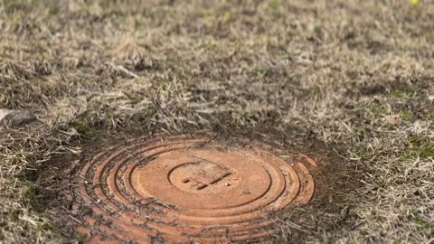 A rusty iron hatch with a pattern covered dirt above an observation well is 库存影片 300052843