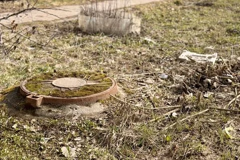 A rusty iron hatch with a pattern covered moss above an observation well is Stock Photos