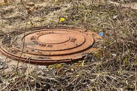 A rusty iron hatch with a pattern covered dirt above an observation well is Stock Photos