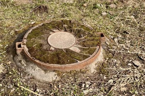 A rusty iron hatch with a pattern covered moss above an observation well is Stock Photos