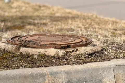 A rusty iron hatch with a pattern covered dirt above an observation well is Stock Photos