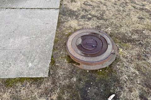 A rusty iron hatch with a pattern is located next to a dry grass pedestrian road Stock Photos