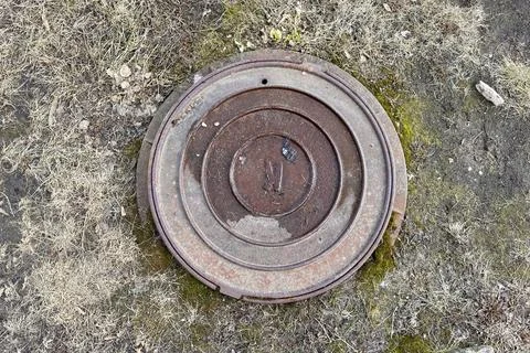 A rusty iron hatch with a pattern is located next to a dry grass pedestrian road Stock Photos