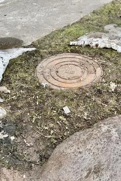 A rusty iron hatch with a pattern is located next to a dry grass pedestrian road Stock Photos