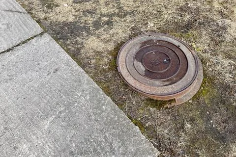 A rusty iron hatch with a pattern is located next to a dry grass pedestrian road Stock Photos
