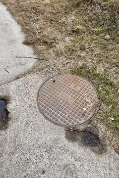 A rusty iron hatch with a pattern is mounted in the asphalt pavement of the Stock Photos