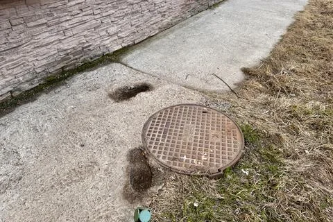 A rusty iron hatch with a pattern is mounted in the asphalt pavement of the Stock Photos