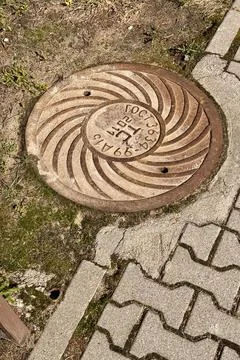 A rusty iron hatch with a pattern is mounted in the asphalt pavement of the Stock Photos