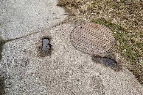 A rusty iron hatch with a pattern is mounted in the asphalt pavement of the Stock Photos