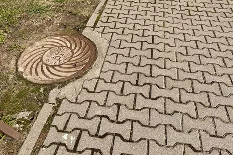 A rusty iron hatch with a pattern is mounted in the asphalt pavement of the Stock Photos