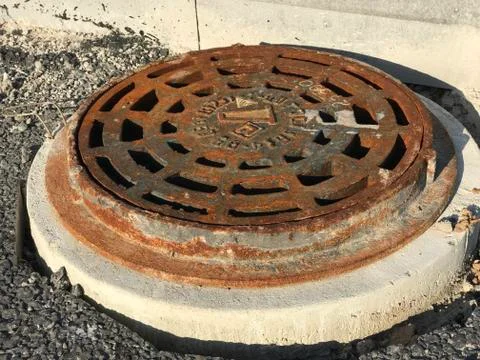 Rusty iron manhole set into asphalt road surfaces Stock Photos