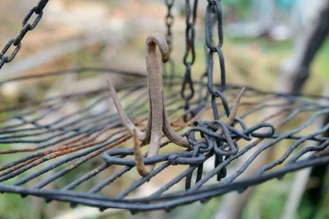 Rusty iron triple hook on grate hanging on chains. Shallow depth of field. Stock Photos