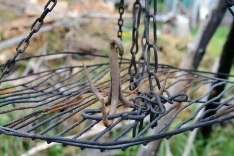Rusty iron triple hook on grate hanging on chains. Shallow depth of field. Stock Photos
