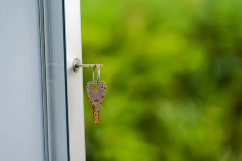 Rusty keys in white window one inserted and one hanging Stock Photos