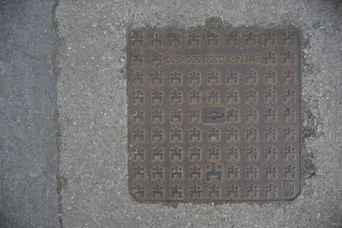 Rusty manhole cover featuring pixel art in Cremona, Italy Stock Photos