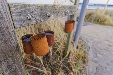 Rusty metal cans hanging on wire hooks along old wooden fence Stock Photos