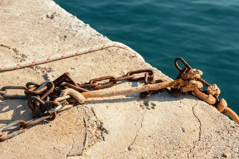Rusty metal chain and thick mooring rope secured on a concrete pier by the se Stock Photos