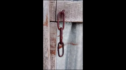 Rusty metal chain links hanging from a rough wooden gate structure close up 스톡 동영상 336802503