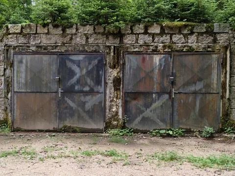 Rusty metal doors embedded in weathered stone wall under dense greenery, mo.. Stock Photos
