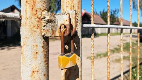 Rusty metal gate with yellow padlock secured, showcasing weathered texture Stock Photos