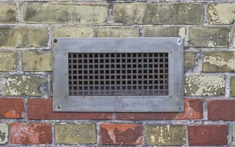 A rusty metal grid is built into a wall, which has a wide steel frame Stock Photos