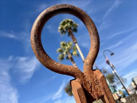 Rusty metal loop in focus with blurred palm trees and blue sky behind Foto stock