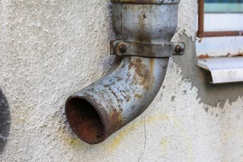 Rusty metal pipe attached to a wall with peeling paint in urban setting Stock Photos