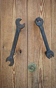 Rusty metal wrenches function as doorknobs on a weathered wooden door in a .. Stock-Fotos