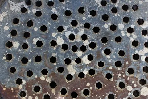 Rusty metallic gray surface with brown splashes. hexagonal holes in wall Foto stock