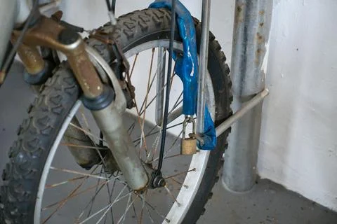 Rusty old bicycle front wheel locked and secured to metal bike stand. Stock Photos