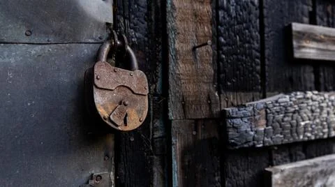 A rusty old padlock is hanging on an old wooden door, creaking softly Stock Photos