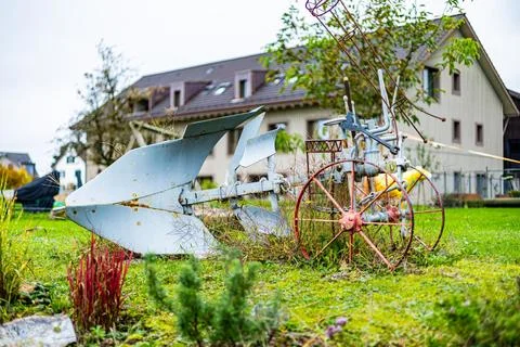 A rusty old plow is sitting in a yard next to a house. Stock Photos