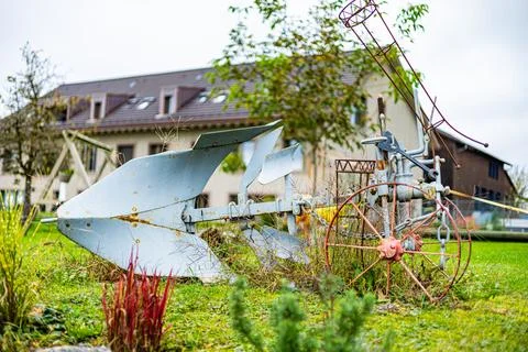 A rusty old plow is sitting in a yard next to a house. Stock Photos