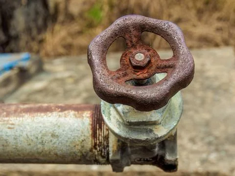 A rusty old water valve attached to a pipe, in a yard near the church of the  Stock Photos