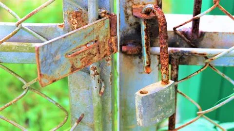 A rusty padlock securing two metal fence posts. The padlock is heavily corroded Stock Photos
